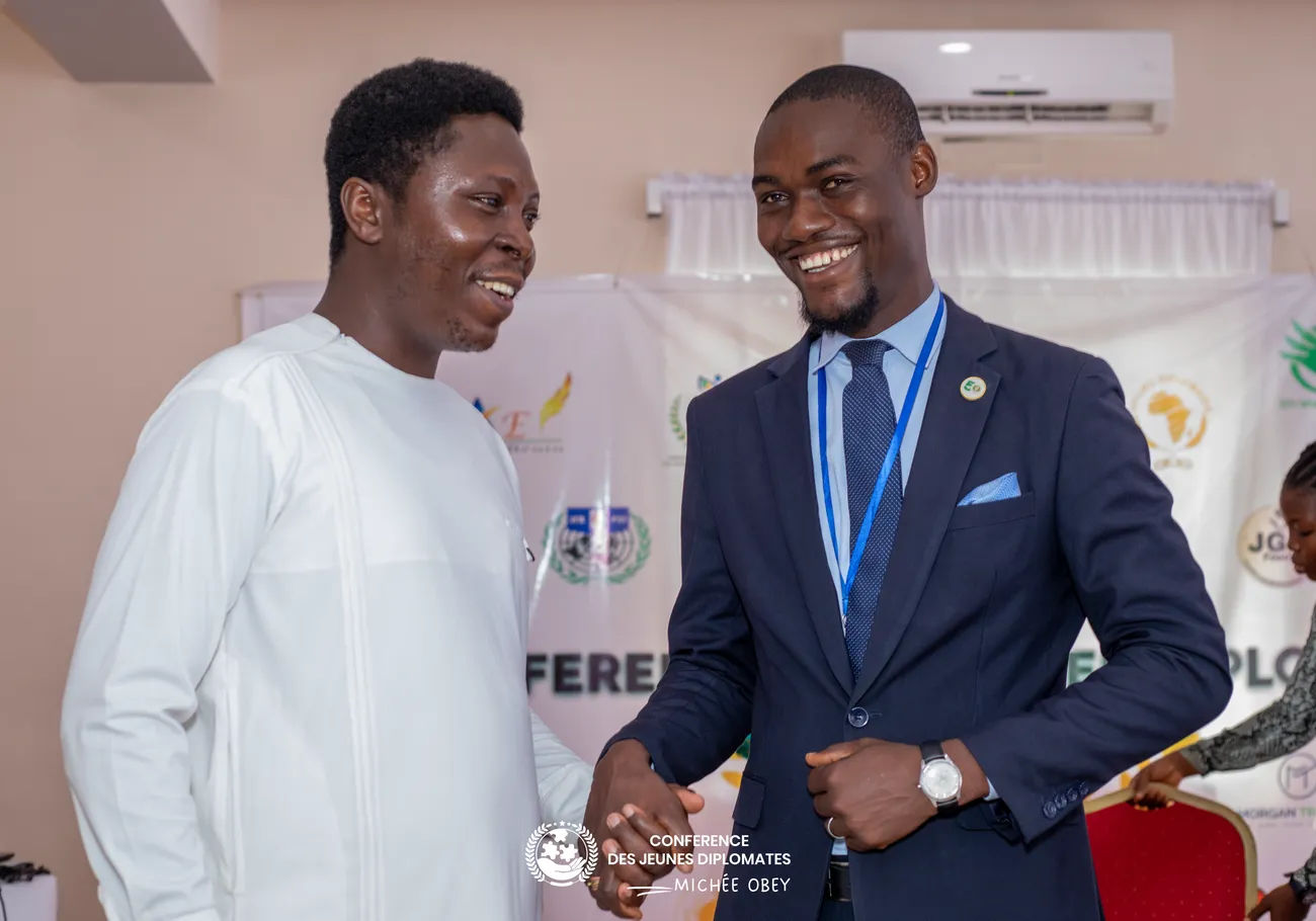Deux jeunes diplomates souriants devant la bannière de la COJED